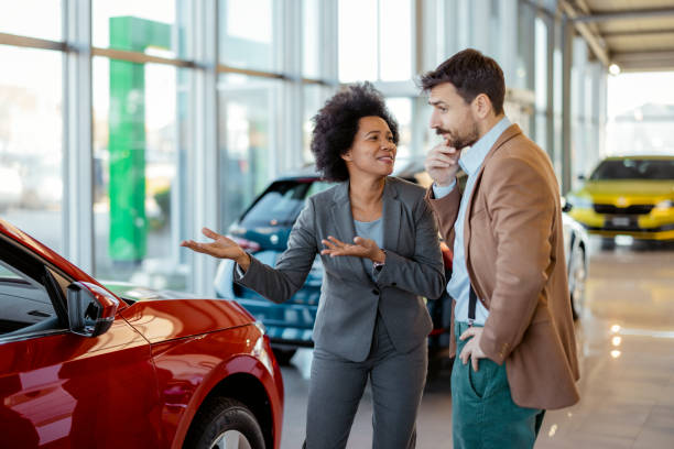 woman desiring an expensive car in a show room, with a worried looking husband