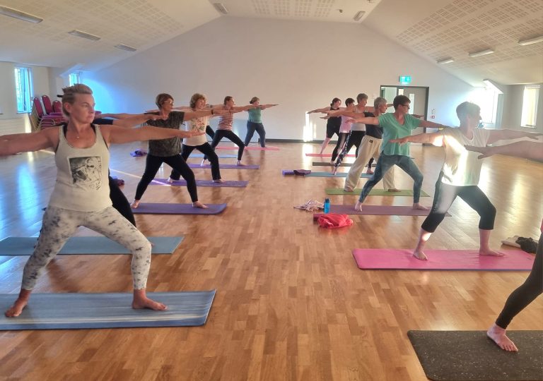 yoga class in large hall with students in standing yoga pose.